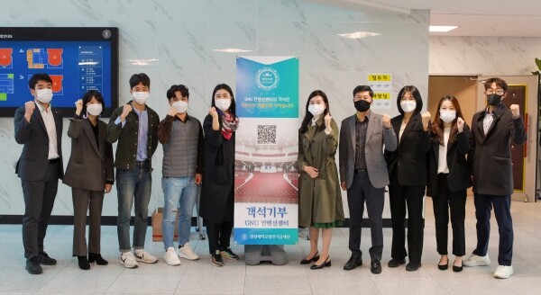 경상대 관계자들이 GNU컨벤션센터 객석기부 홍보 전단 표지 앞에서 기념사진을 촬영하고 있다. (사진=경상대 제공)