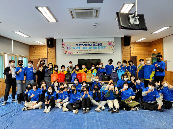 원광보건대 미용피부화장품과 학생동아리 동그라미 학생들이 봉사활동 후 마을 주민들과 함께 기념촬영하고 있다. 사진=원광보건대 제공